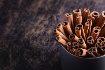 Cinnamon sticks in ceramic bowl on black rustic background with copyspace.