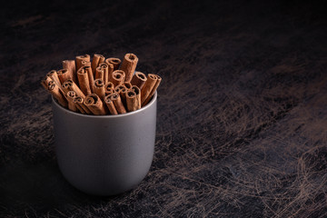 Cinnamon sticks in ceramic bowl on black rustic background with copyspace.