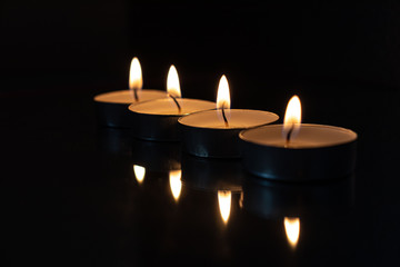 four candles lined up with dark background showing the light of the fire and the reflection in the mirror