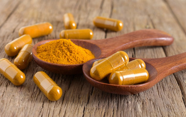 Close up,Capsules and turmeric (curcumin) powder in a spoon on the wooden background. 