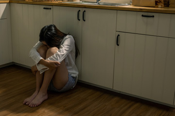 Depressed young beautiful Asian woman sitting on kitchen floor with hugging knees. Loneliness sad teenage girl living alone at home and cry. Mental health, drug abuse and social issue concept.