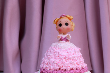 Princess doll cake with dress made of cream on pink curtain background.