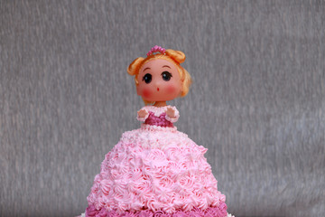Princess doll cake with dress made of cream on grey background.