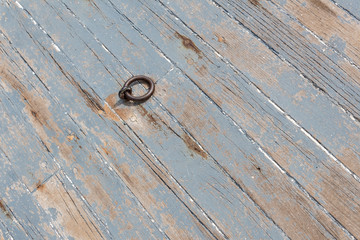 Rusted iron ring in a weathered wood boat deck, peeling gray paint, copy space, horizontal aspect