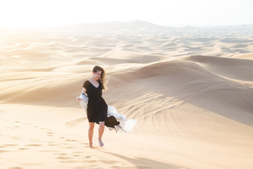 A girl in a black long dress walks through the desert Caucasian young beautiful girl alone is in a hot waterless desert. Runs along sandy mountains and dunes