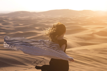 Running to meet the rising sun. A girl with long hair in a black dress runs into the sunlight in the desert