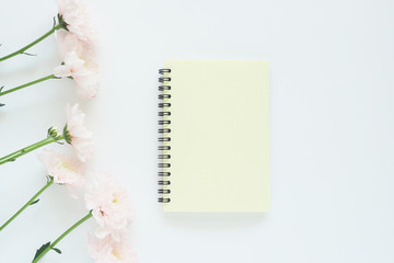 .mock up yellow notebook on a spring and six soft pink chrysanthemums on a white background. Space for text..