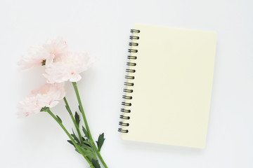 yellow notebook on a spring and three pink chrysanthemum flower on a white table...
