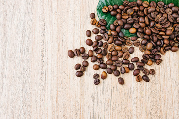Coffee beans on a green leaf and scattered on a light wooden table, top view, closeup grains, flat lay, place to insert text, copy space