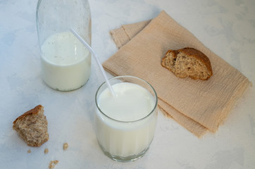 Close-up glass of milk, a half-empty milk bottle and broken whole grain bread on a linen napkin on a light surface. Healthy food, useful snack is a concept. Horizontal orientation, selective focus.