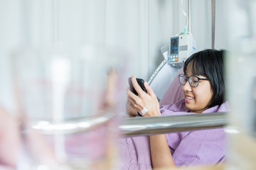 A sick girl in a purple dress with a smartphone attached to a lifesaver in a hospital bed