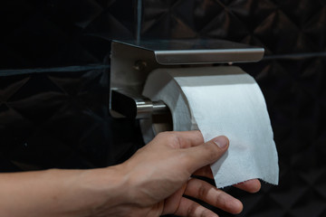 Young man sitting in water closet at home.Using toilet paper.