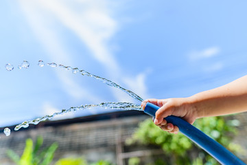 The boy is holding a hose to spray water on the tree. He tried to use his little finger to cover the pipe a little to increase water pressure. What happened makes him enjoy the watering of plants.