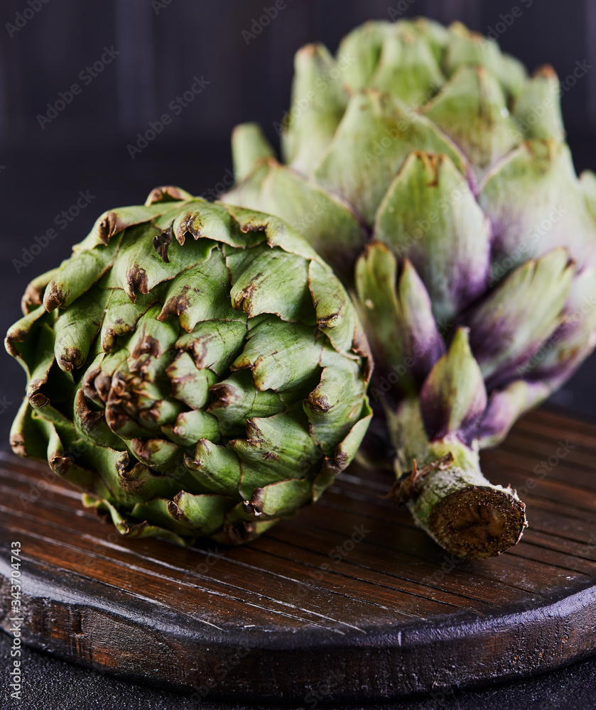 Poster Fresh artichokes on a wooden stand against a dark background