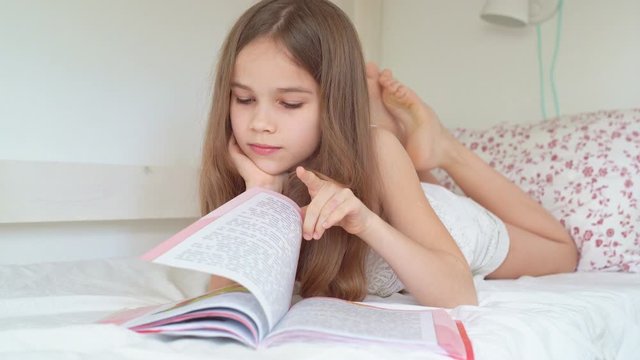school concept. little girl with book lying on bed