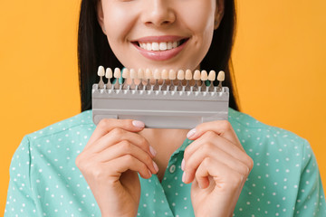 Beautiful young woman with teeth color samples on color background, closeup
