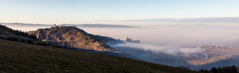 Fototapeta na wymiar A panoramic, epic view of St.Francis church in Assisi town (Umbria) above a sea of fog at dawn