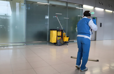 Closeup of woman worker cleaning floor with janitorial, cleaning equipment and glass wall background.