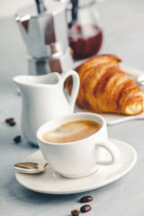 Coffee espresso in white cup with milk, jam and croissants.