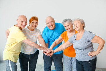 Happy elderly people putting hands together in gym