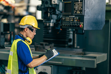 Asian engineer checking the machine in factory, worker writing note with list paper.