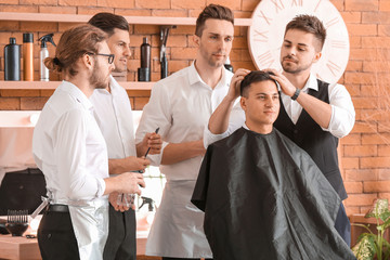 Professional hairdresser teaching young men in salon