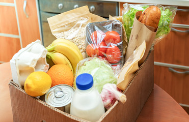 Close-up cardboard box with different fresh packed food products on kitchen table. Safe delivery. Selective focus.