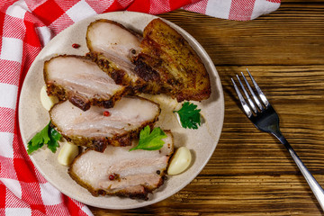 Baked pork belly in a plate on wooden table. Top view