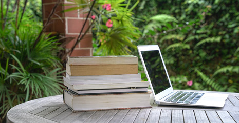 Stacked of books next to computer laptop. Garden view.