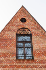 Fototapeta na wymiar brown wooden window with forged vintage bars on the background of the old red, brick wall and the roof of the Catholic Church