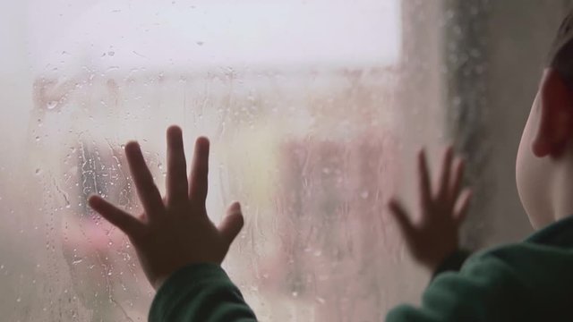 Little kid toddler playing with condensation on a glass door looking and missing the street and playing outdoors after spending many weeks in lockdown at home due to virus