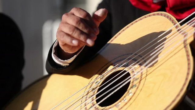 Mariachi band member strumming his brown acoustic guitar.