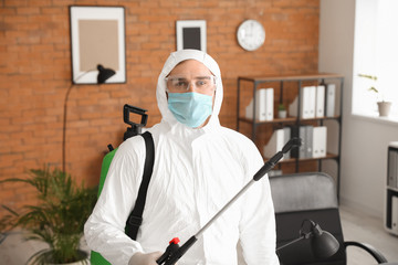 Fototapeta na wymiar Worker in biohazard suit disinfecting office
