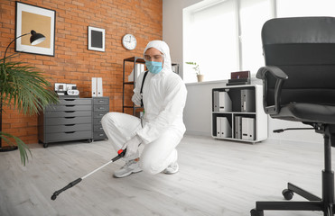 Worker in biohazard suit disinfecting office - obrazy, fototapety, plakaty