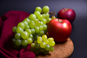 Green grapes with two red apples on a dark background.