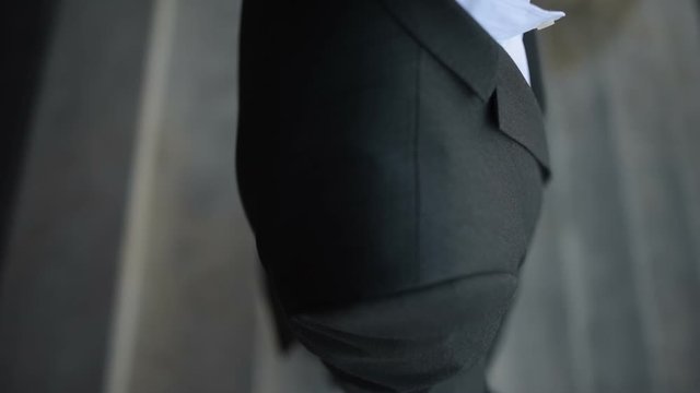 Man in custom tailored suit posing outdoors and buttoning his jacket.