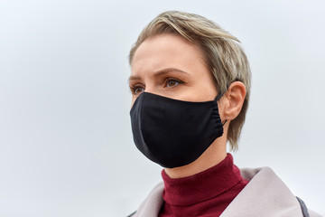 health, safety and pandemic concept - young woman wearing black face protective reusable barrier mask outdoors