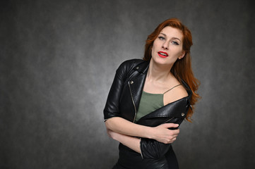 Pretty Model with great makeup posing on a gray background in the studio. Horizontal portrait of a red-haired young woman in a black jacket and green t-shirt.