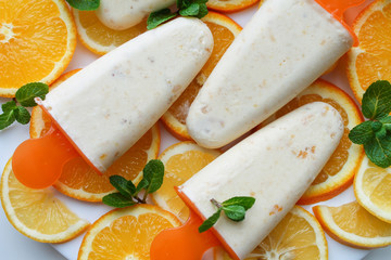 Homemade natural orange popsicles or ice cream with mint on white plate background. Top view, macro