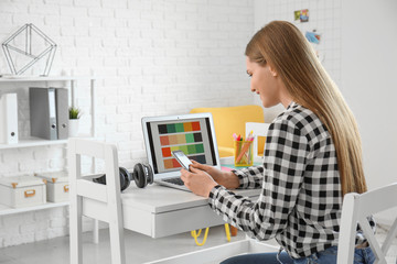 Young female designer with laptop and mobile phone working at home