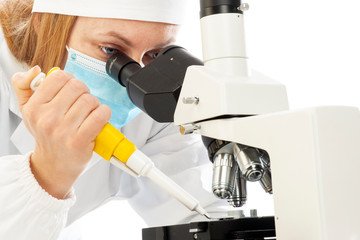 A scientific researcher wearing a surgical mask who is doing microscopic tests