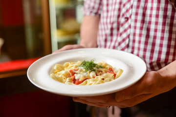 A waiter holds a plate of tasty food. Italian cuisine in restaurant, Pasta with sauce and parmesan cheese.