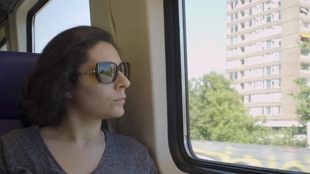 Thoughtful Woman with Brown Sunglasses Looking out Train Window on Sunny Day