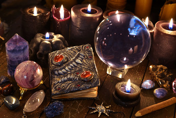 Crystal ball, magic book and burning black candles on witch table.