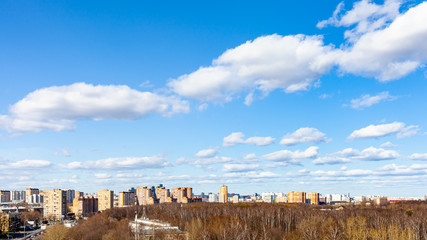 blue sky with white cumulus clouds over city street and park on sunny March day
