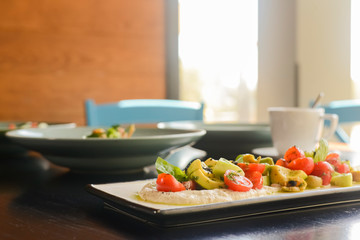 Fresh vegetables and green salad with sauce served on traditional rectangular white plate over dark wooden background