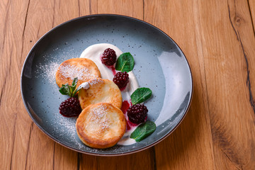 Tasty sweet cheese pancakes with sauce served on a plate over dark rustic wooden background. Banner with copy space.