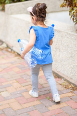 Kid taking out the separate garbage. Back view little girl holding plastic water bottles for recycling. Concept plastic free world the future for our children. Zero waste.
