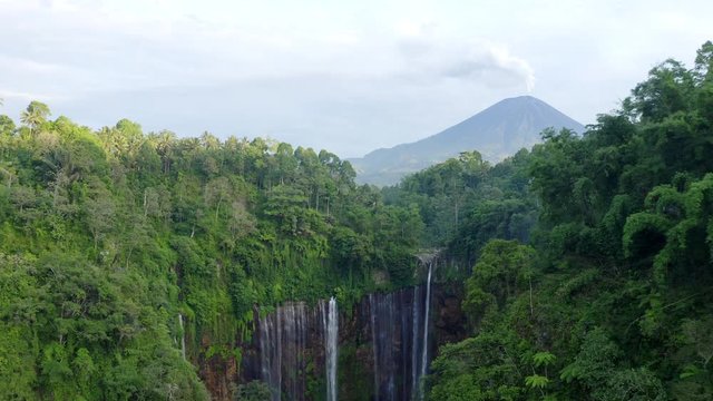 Tumpak Sewu waterfall hidden in East Java jungle, erupting volcano in distance