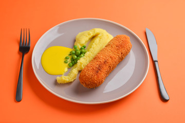 Cordon bleu cutlet, deep fried meat served with mashed potatoes and green peas on gray plate over orange background.